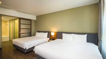 Quarto de hotel com duas camas, um banheiro e uma mesa de cabeceira com abajur.