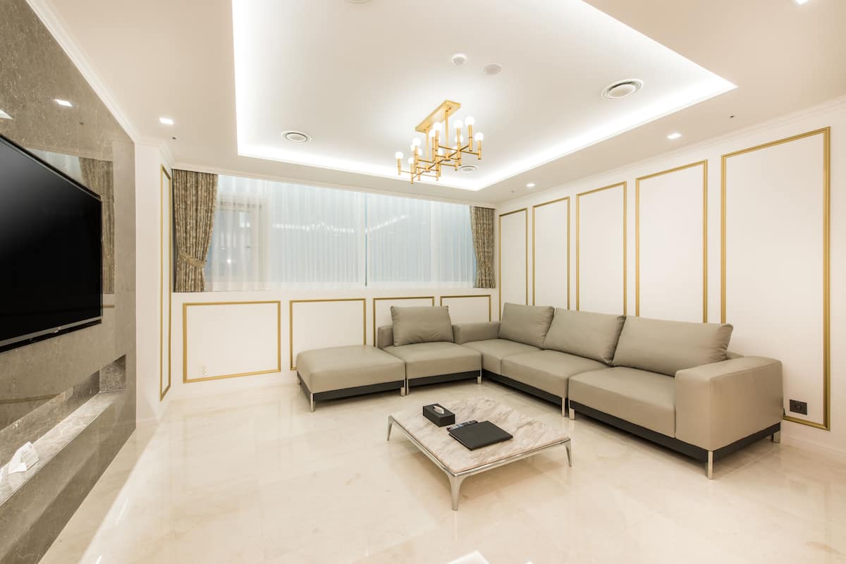 A modern living room with a sectional sofa, a flat-screen TV mounted on the wall, and a marble coffee table.