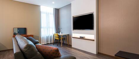 A modern living room with a sofa, a TV mounted on the wall, and a dining area with a table and chairs.