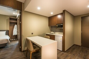 Een compacte hotelkamer met een bed, een eettafeltje, een kitchenette en een eigen badkamer.