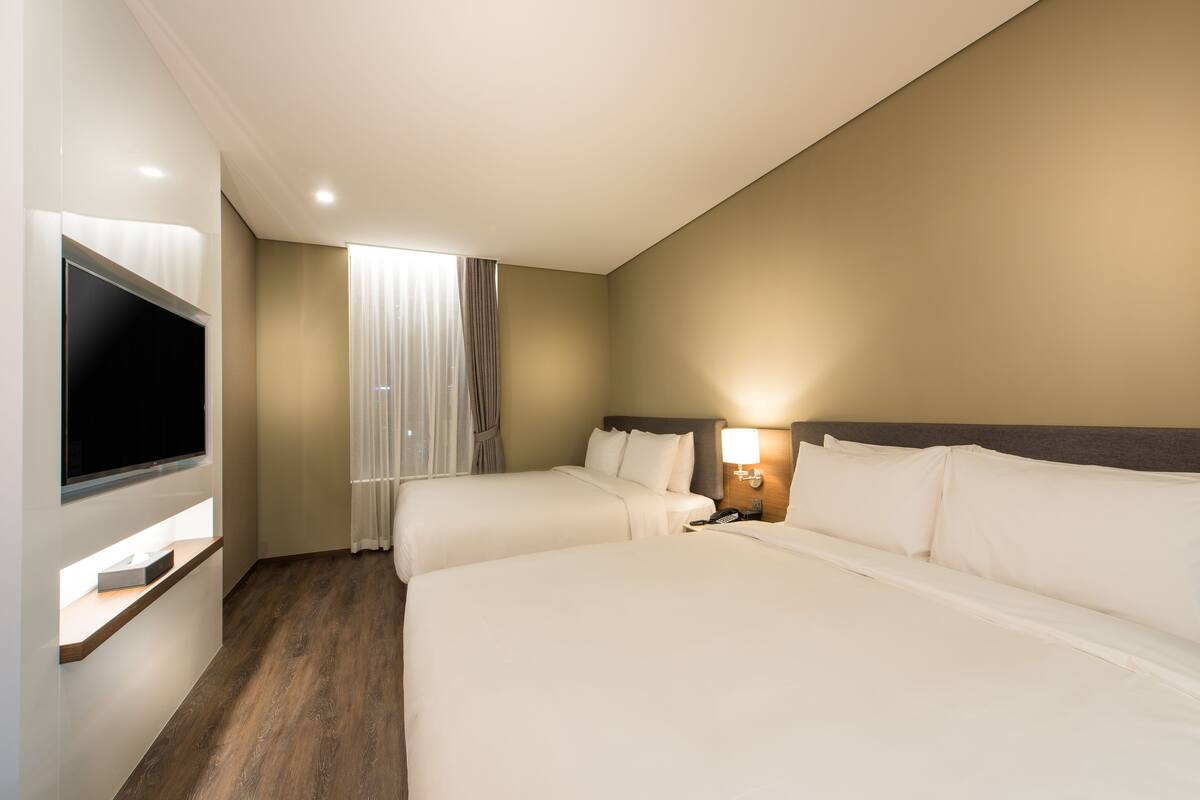 A hotel room with two beds, a TV, and a window with curtains.