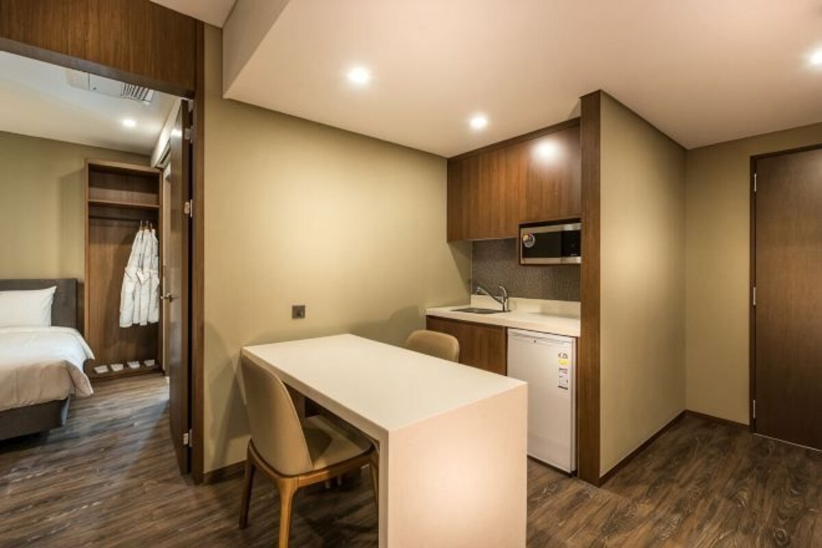 Habitación de hotel compacta con una cama, una pequeña mesa de comedor, un microondas y una lavadora.
