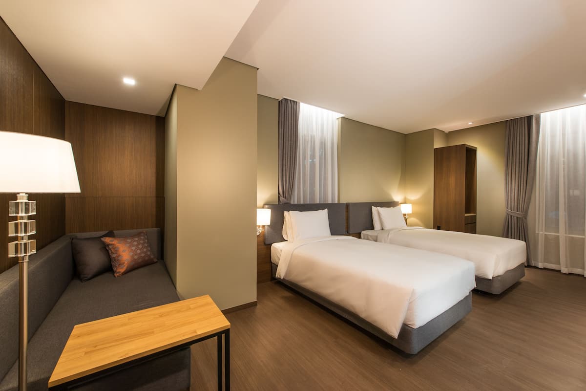 A hotel room with a sofa, two beds, a wooden table, and a nightstand.