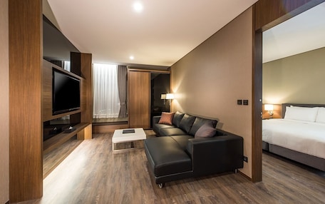 A modern hotel room with a flat-screen TV, a sofa, a bed, and a wooden floor.