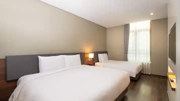 Ein Hotelzimmer mit zwei Betten, einem Holzkopfende, einem Nachttisch mit Lampe, einem Fenster mit Vorhängen und einem an der Wand befestigten Flachbildfernseher.