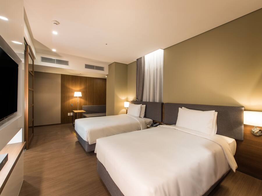 A hotel room with two beds, a TV, a desk, and a lamp.