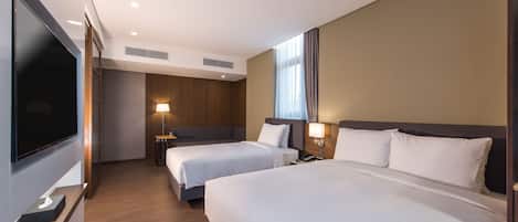 A hotel room with two beds, a TV, a desk, and a lamp.