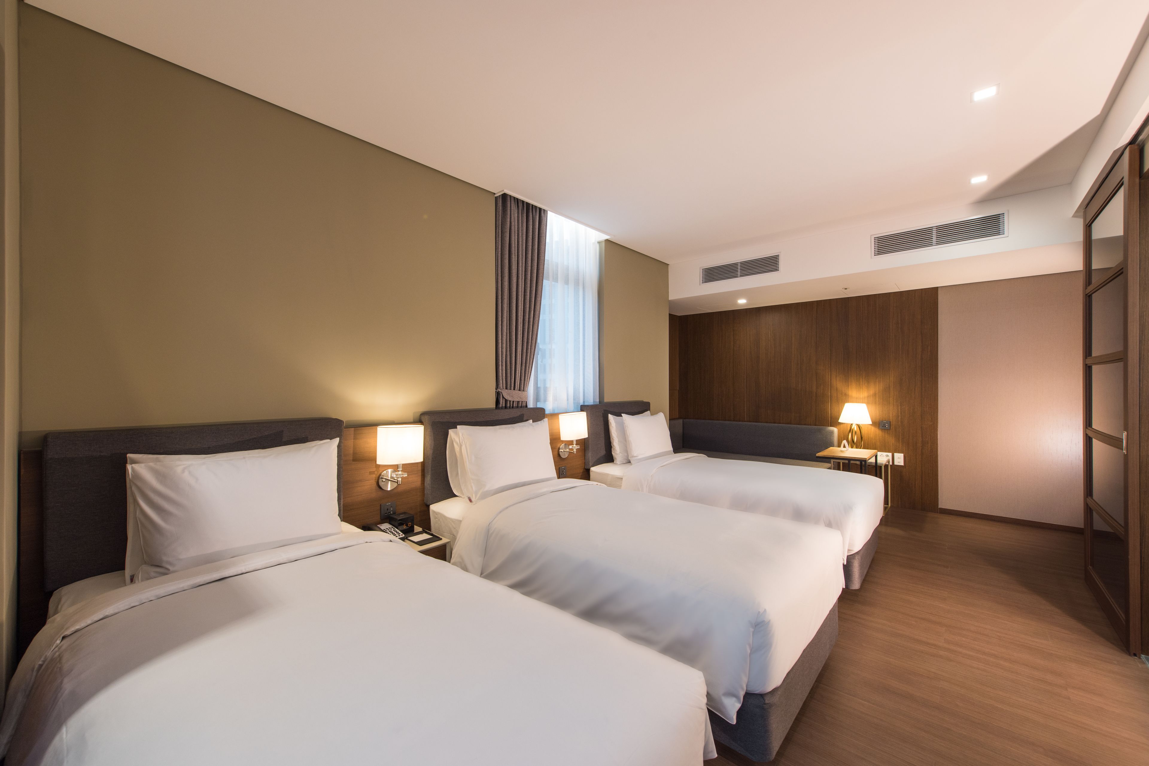 A hotel room with three beds, wooden headboards, and bedside lamps.
