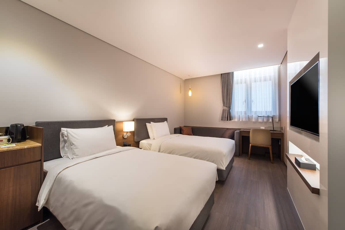 A hotel room with two beds, a desk, a TV, and a coffee machine.