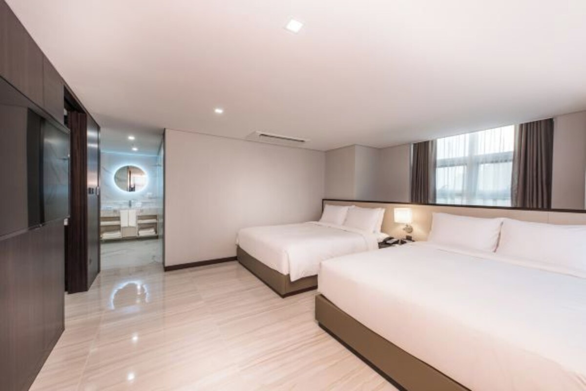 Habitación de hotel con dos camas, un baño con un espejo redondo y vistas a la ciudad.
