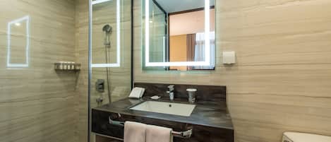 Un baño moderno con tocador de mármol, cabina de ducha de vidrio y un espejo grande con iluminación integrada.
