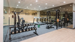 Une salle de sport équipée de tapis de course, d’appareils de musculation et d’un porte-haltères.