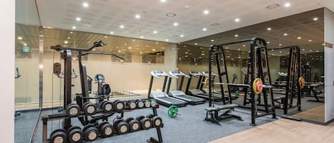 Un gimnasio con cintas de correr, máquinas de pesas y un estante con mancuernas.