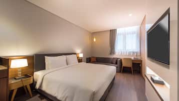 Habitación de hotel con una cama grande, un escritorio, una silla, un televisor y una ventana con cortinas.