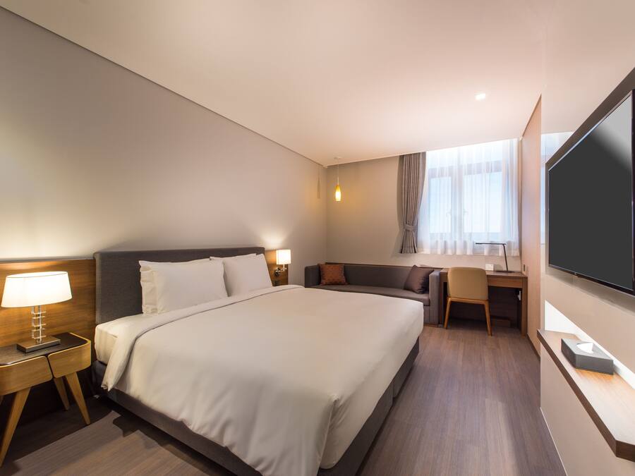 Habitación de hotel con una cama grande, un escritorio, una silla, un televisor y una ventana con cortinas.