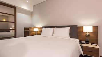 A neatly made bed with white linens, two bedside lamps, and a nightstand with a phone and a digital clock.