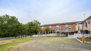 Un edificio con fachada de ladrillo, camino de grava y patio cercado.
