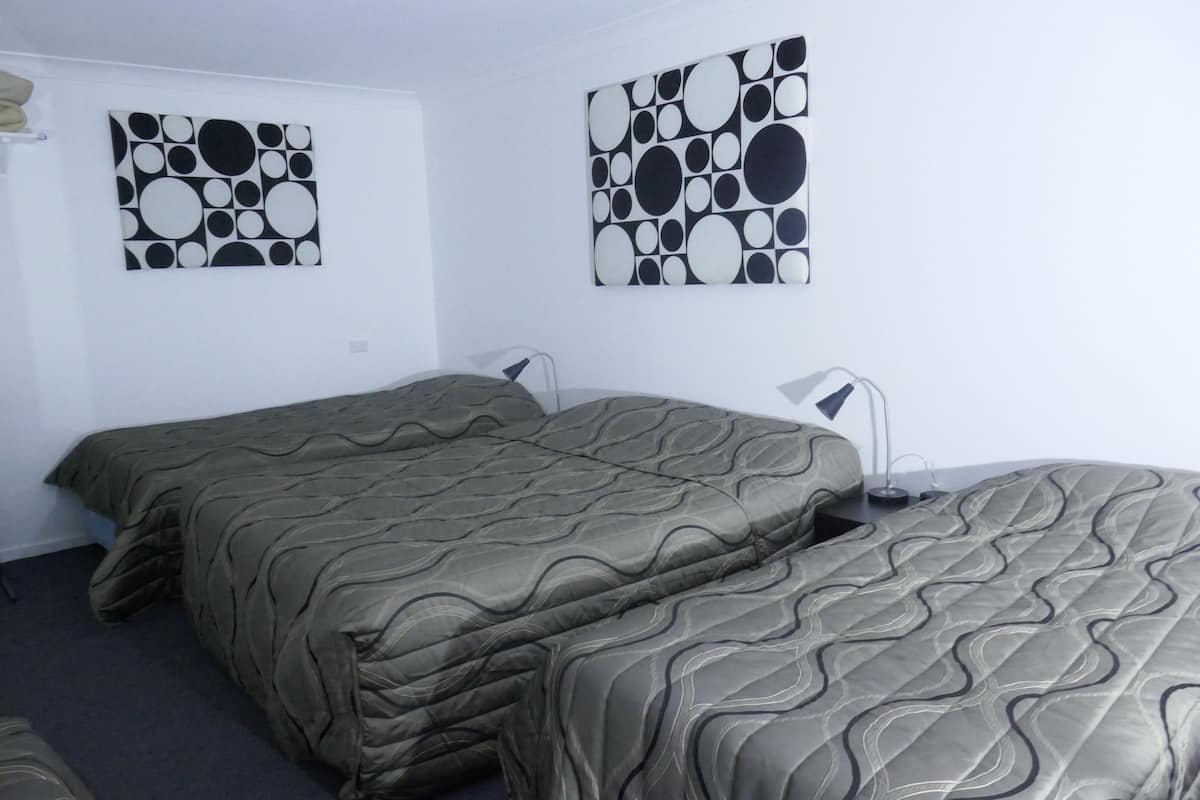 A hotel room with two beds, a wall-mounted lamp, and two abstract paintings.