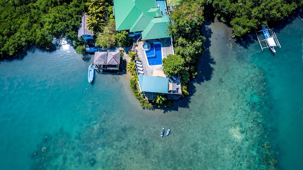 An aerial view of a tropical island resort with a swimming pool, a boat dock, and clear turquoise waters. - Edgewater Dive & Spa Resort (Puerto Galera)