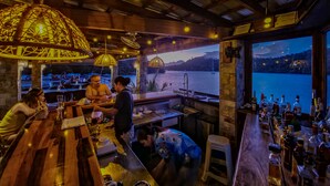A bar area with a view of a lake and mountains, wooden furniture, and hanging lamps. - Edgewater Dive & Spa Resort (Puerto Galera)