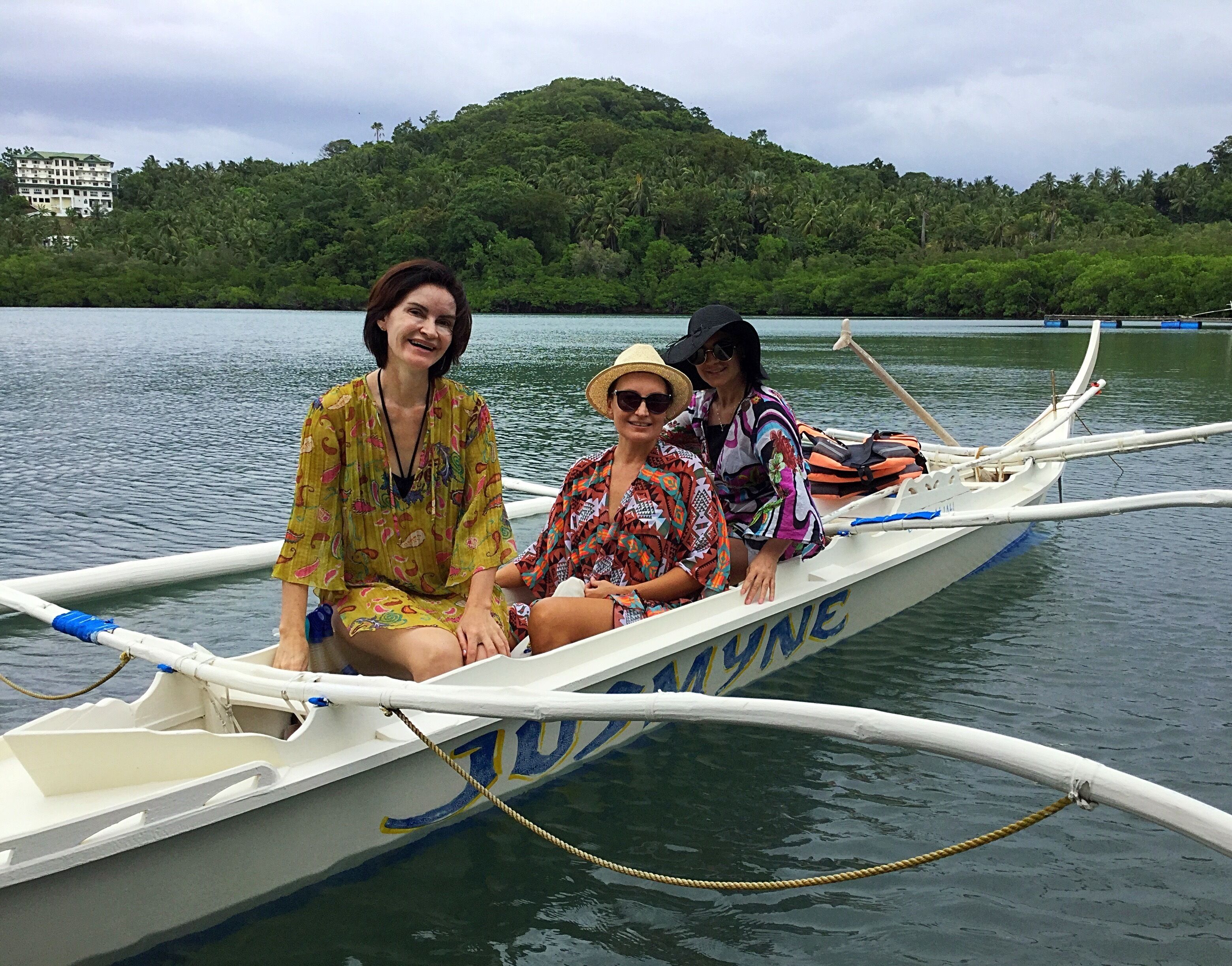 A boat with the name "BAYLINE" on its side, three people sitting on it, and a forested hill in the background.