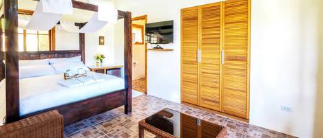 A bedroom with a large bed, wooden wardrobe, and a television on the wall.
