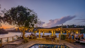An outdoor dining area with a pool, surrounded by trees and overlooking a body of water. - Edgewater Dive & Spa Resort (Puerto Galera)