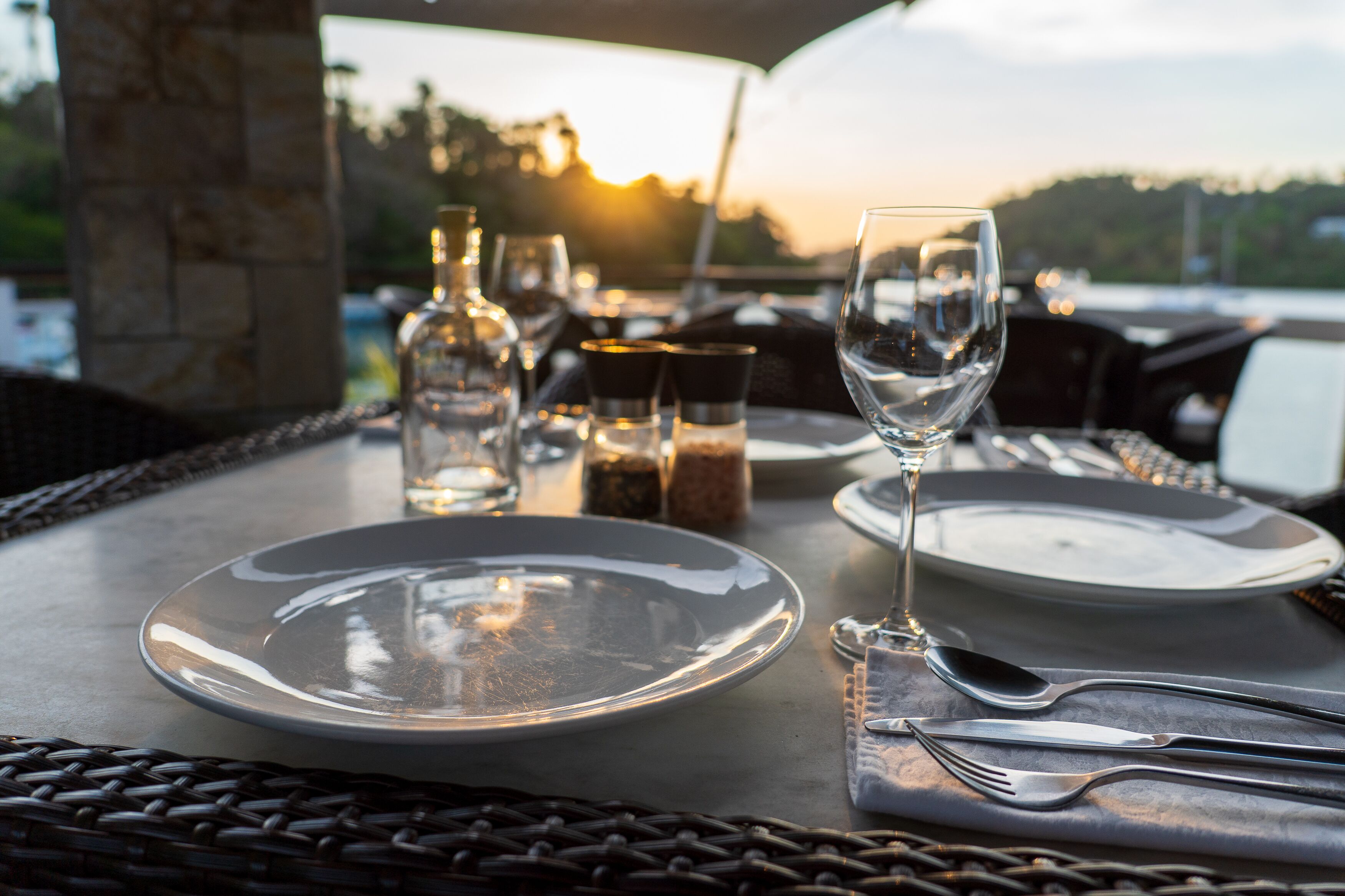Una mesa lista para comer, con platos, cubiertos y vasos, con vistas a un paisaje pintoresco.