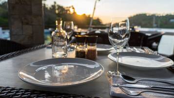 Una mesa lista para comer, con platos, cubiertos y vasos, con vistas a un paisaje pintoresco.