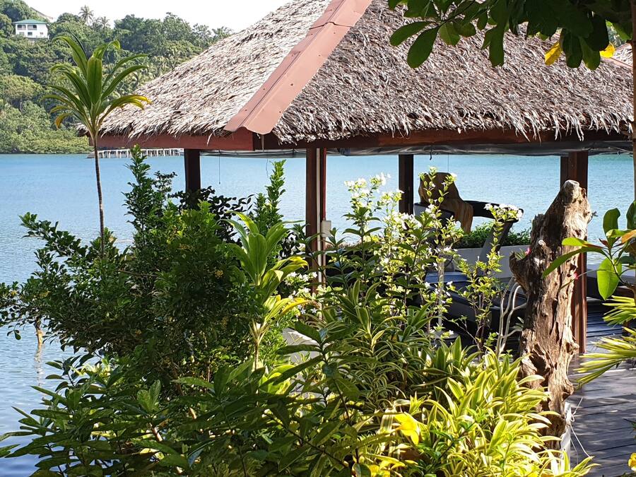 A thatched-roof structure with a view of a calm lake and lush greenery.