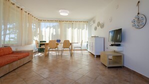 Un salon comprenant un canapé, une table à manger, des chaises, un téléviseur et un meuble.