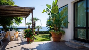 Une terrasse avec des meubles d’extérieur, une grande plante en pot et une vue sur la mer.