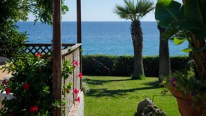 Un jardin agrémenté d’une pergola en bois, d’un palmier et offrant une vue sur la mer.
