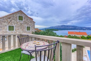 A balcony with a table and chairs, overlooking a body of water and mountains.