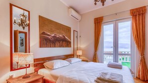 Ein Hotelzimmer mit einem großen Bett, einem Nachttisch, einer Wand-Klimaanlage, einem Gemälde und Blick ins Freie durch ein Fenster.