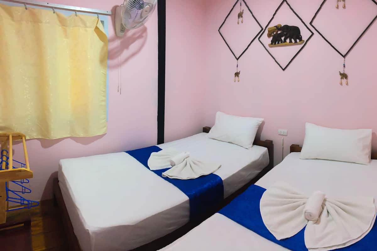A room with two single beds, a fan, a curtain, and wall decorations.
