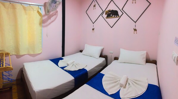 A room with two single beds, a fan, a curtain, and wall decorations.