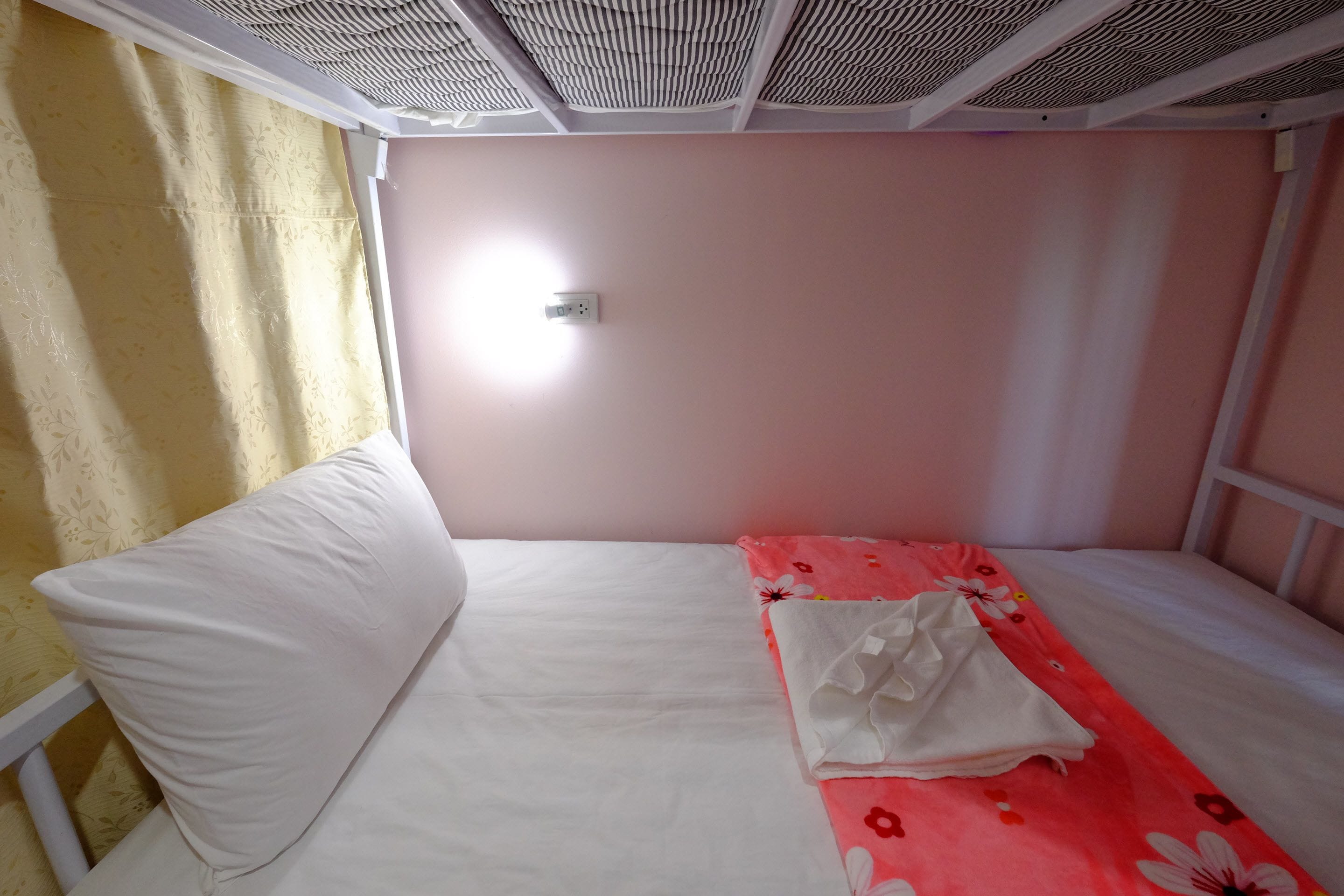A single-bed room with a white mattress, a floral-patterned blanket, and a white pillow.