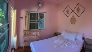 A bedroom with a bed, a drying rack, a window with curtains, a wall fan, and decorative wall art. - Sang Chan Hostel (Koh Lipe)