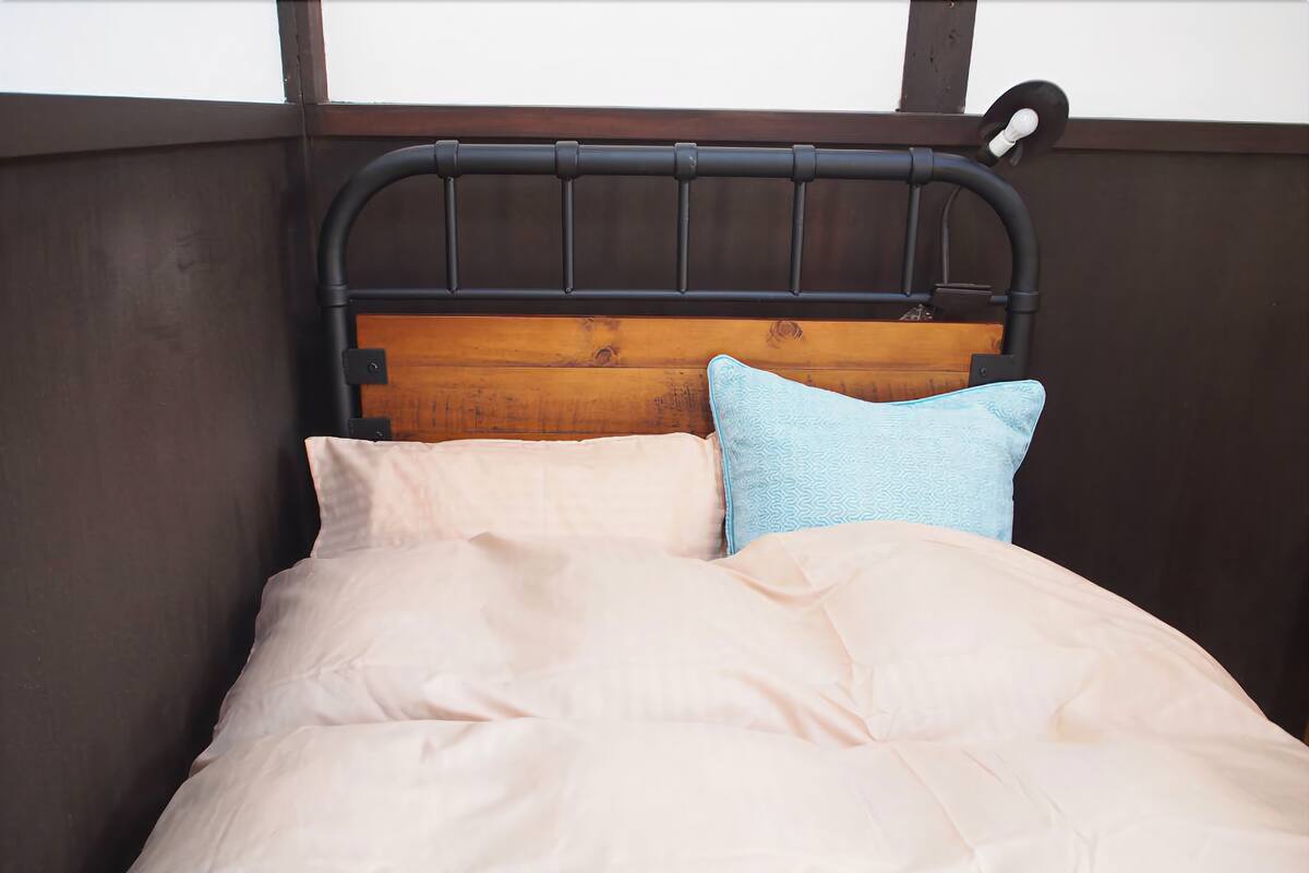 A bed with a wooden headboard, two pillows, and a light-colored bedspread.