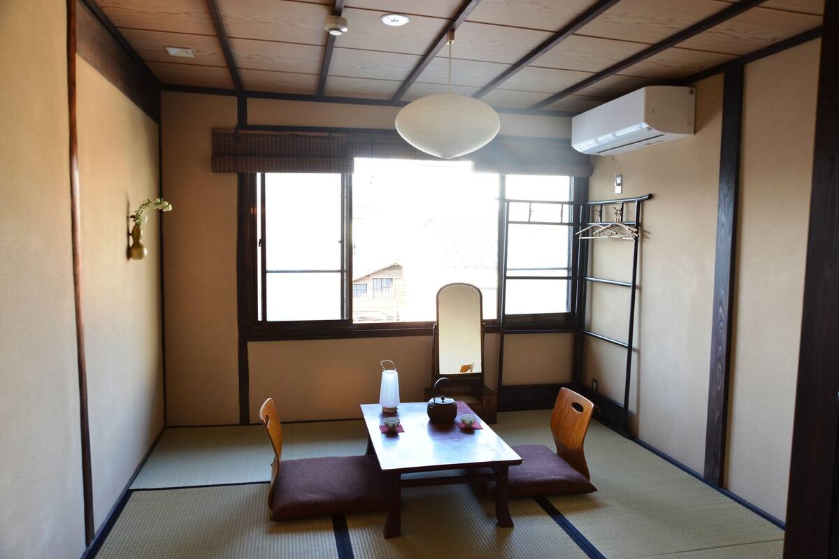 A traditional Japanese room with tatami flooring, a low table with a tea set, and a hanging light fixture.