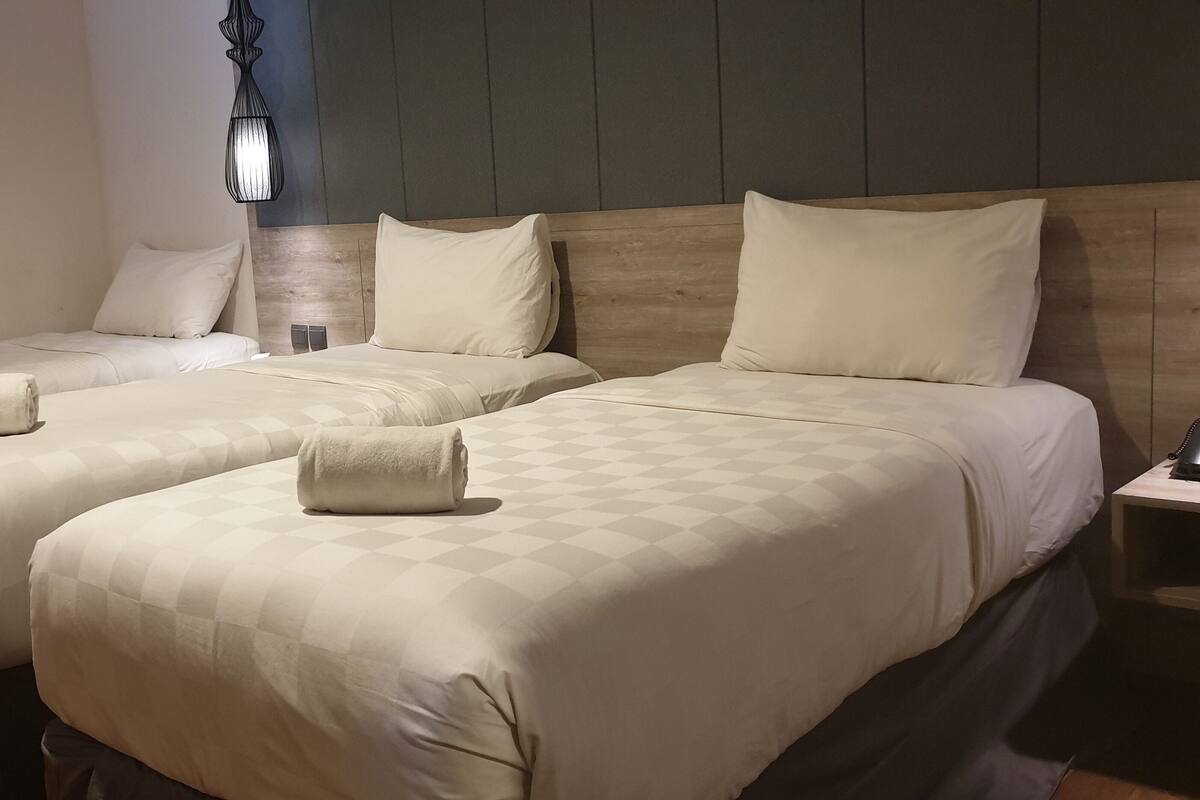 A hotel room with two beds, each with a neatly folded towel and a wooden headboard.