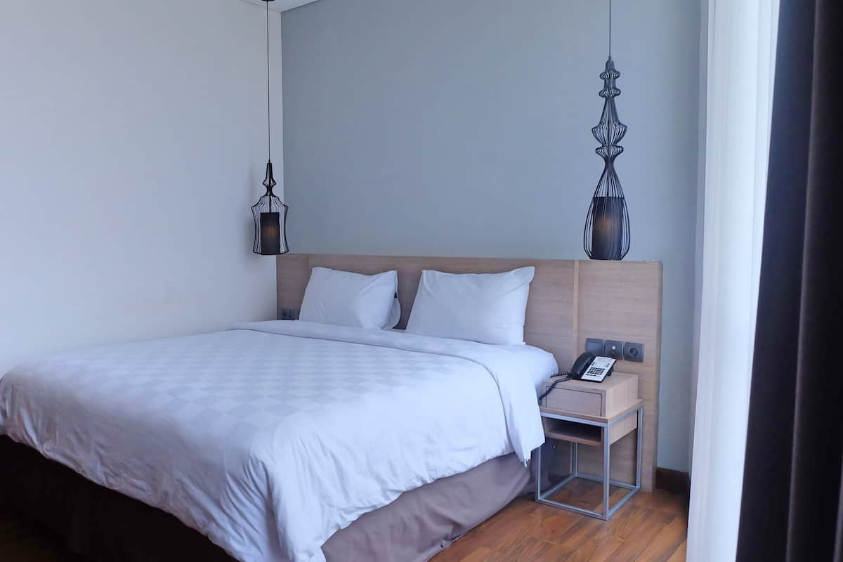 A hotel room with a bed, bedside table, lamp, and a telephone.