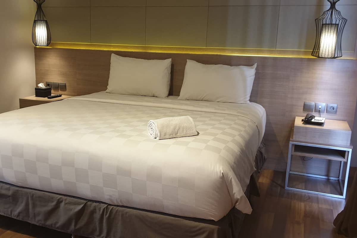 A hotel room with a large bed, two bedside tables, a nightstand, and a wall-mounted lamp.
