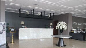 A reception area with a marble counter, two lamps, a vase with flowers, and a framed picture on a stand. - Rivoli Hotel Jakarta (Jakarta)