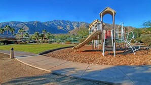 A playground with a slide and climbing structures, surrounded by a landscaped area with a mountain backdrop. - Sunny Palm Springs Solar Oasis 180° Mountains, 30ft Palms & Boulder Desertscape (Palm Springs)