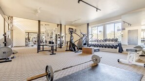 Et fitnesscenter med forskellig træningsudstyr, herunder et løbebånd, styrkemaskiner og håndvægte.