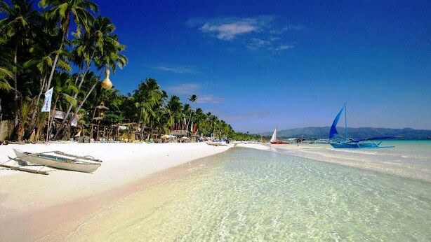 A beach with clear turquoise water, palm trees, and traditional boats. - Aquarius Terraces Boutique Resort (Boracay Island)