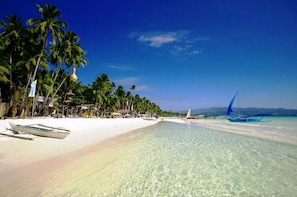 Een strand met helder turquoise water, palmbomen en traditionele boten.