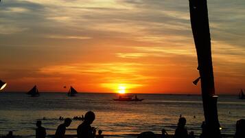Um pôr do sol sobre o oceano com silhuetas de pessoas e barcos.